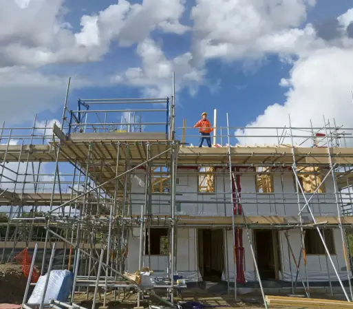 Picture of a half-built house surrounded by scaffolding and a builder standing on the top